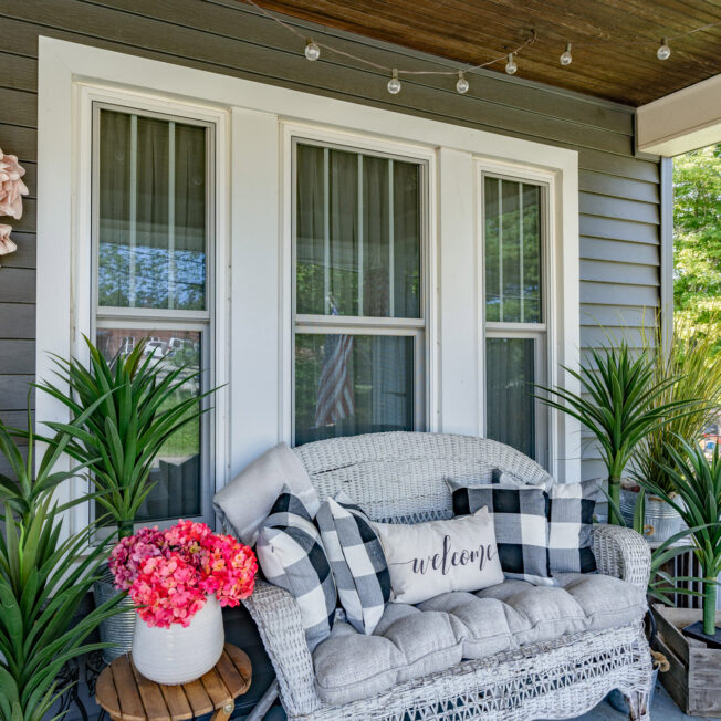 Porch view of a white Aspect™ double hung window with custom grids and a comfortable outdoor sofa beneath the window; example of double hung windows in ProVia's window gallery