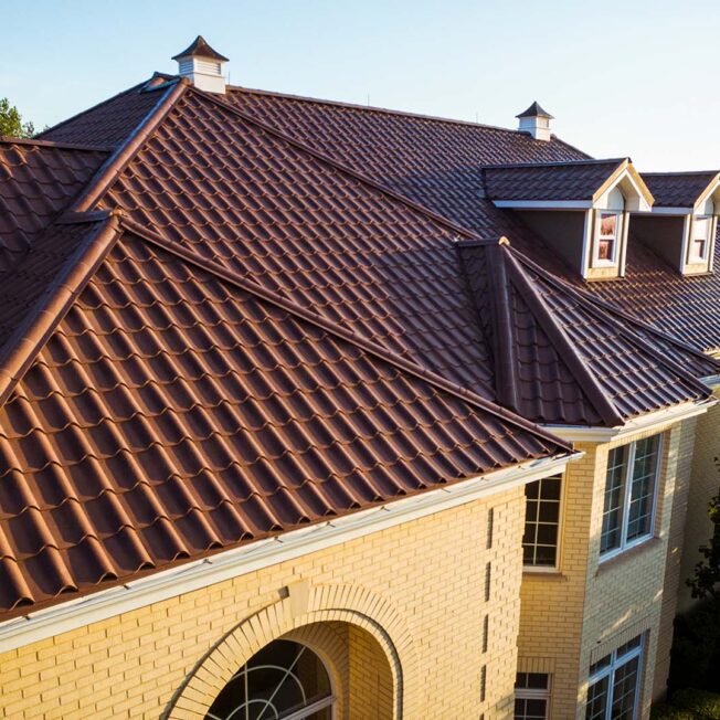 Yellow-toned brick two-story home covered with ProVia's new metal barrel tile roof in Terracotta, example of metal roofing that looks like clay tile