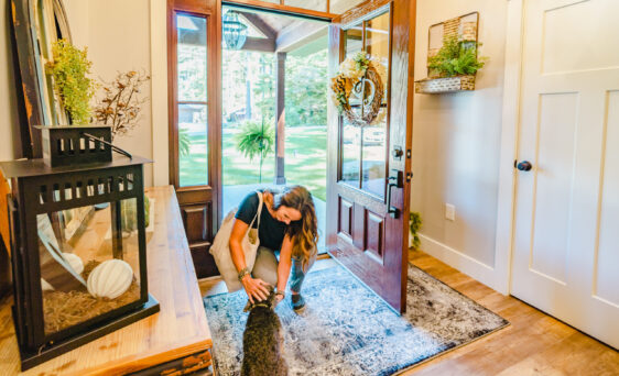 Photo of a woman kneeling down to pet a dog in her entryway, which shows an example of exterior doors with a fiberglass entry door and sidelights, example of ProVia's exterior replacement doors and door exterior options