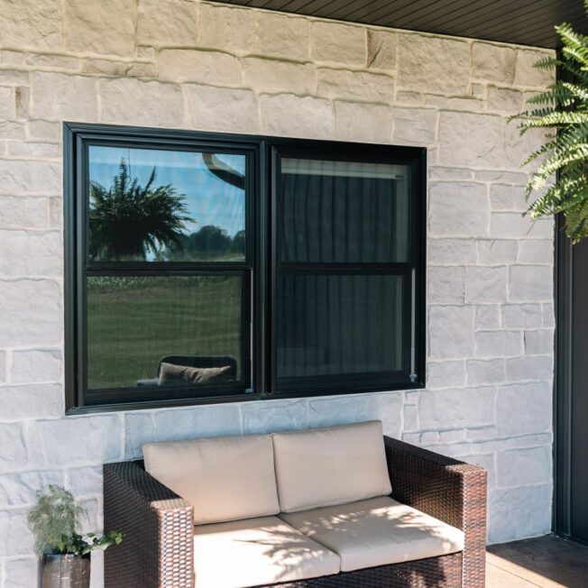 Endure Double Hung windows with clear glass in Coal Black against a white stone home exterior