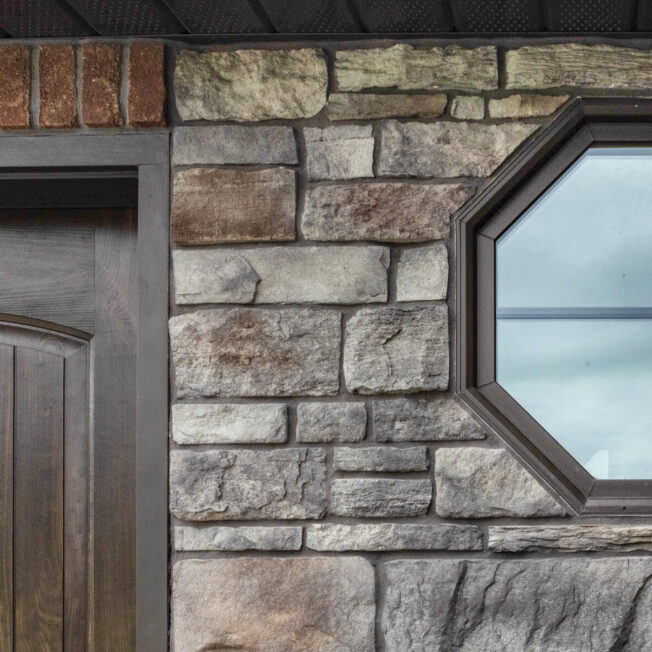 Stone home exterior with octagon windows with Rustic Bronze finish; example of shaped custom home windows in ProVia's window gallery