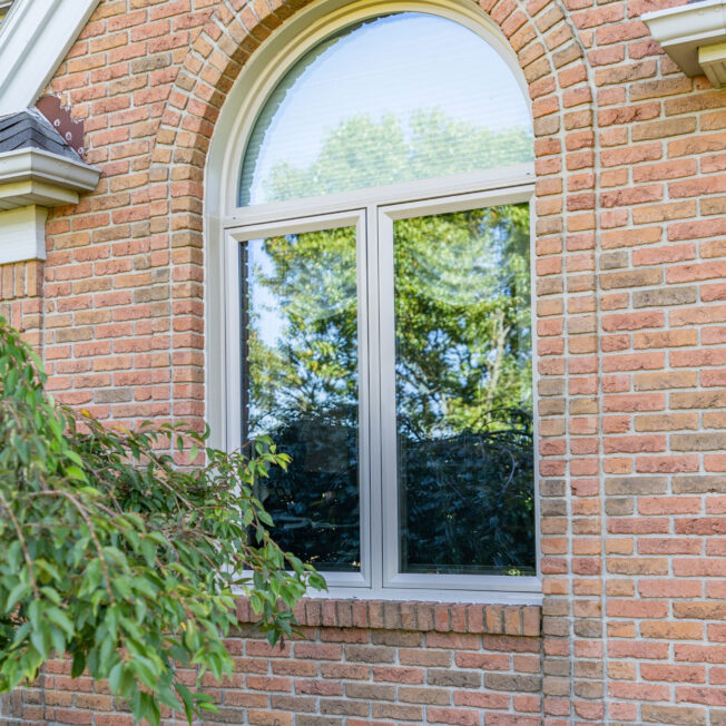 Aeris arch shaped windows in the color beige on a brick home