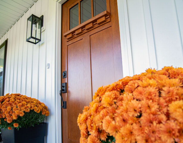 Warm woodgrain stained Signet fiberglass door on a house with white board and batten; front door images example clear glass front door with a dentil shelf