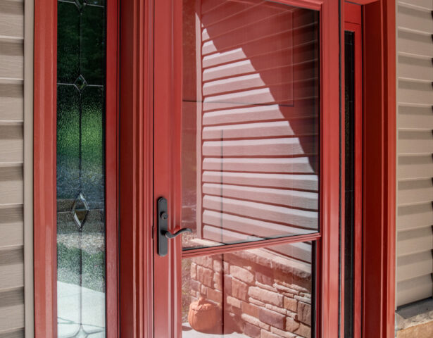 One of ProVia's Spectrum retractable screen doors in Vallis Red over an entry door with sidelites