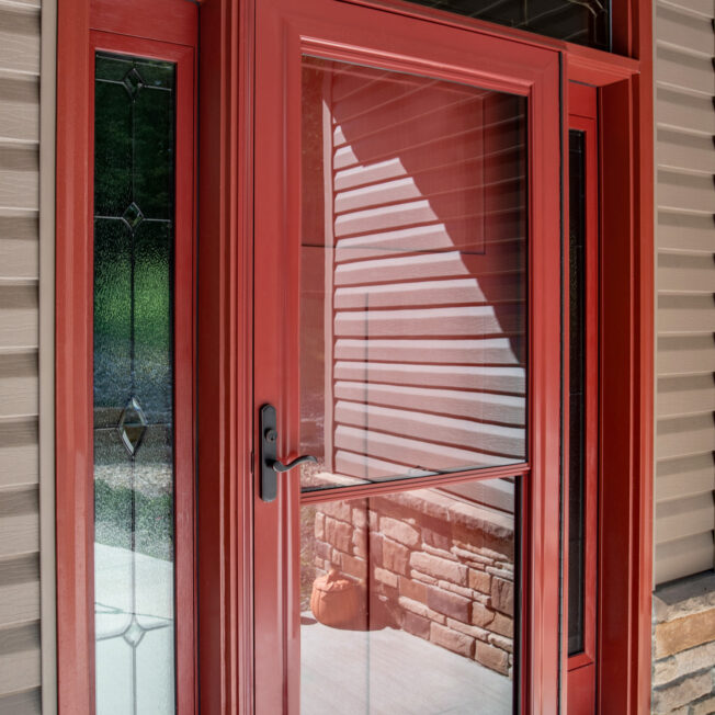 One of ProVia's Spectrum retractable screen doors in Vallis Red over an entry door with sidelites