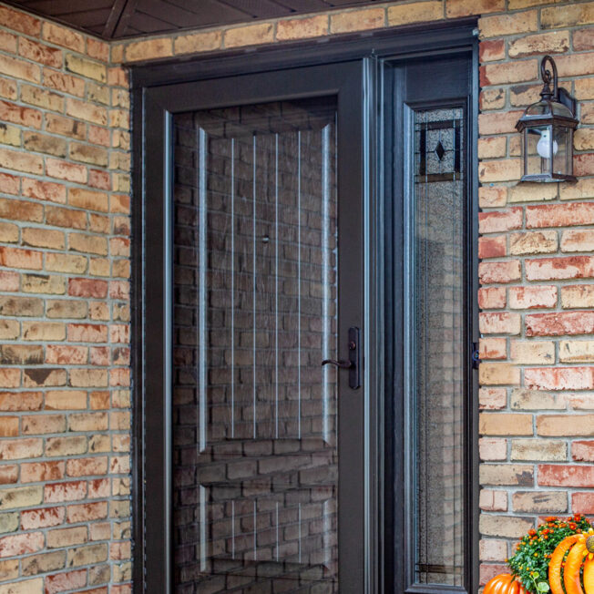 Outside image of a brick home featuring ProVia's Decorator full glass decorative storm door in Rustic Bronze