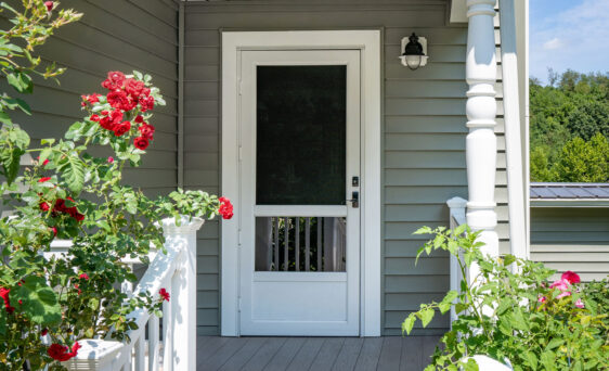 One of ProVia's Deluxe storm doors in White on a porch with red roses spilling over white railings