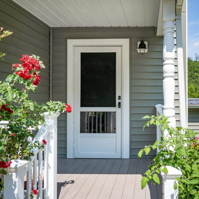 One of ProVia's Deluxe storm doors in White on a porch with red roses spilling over white railings
