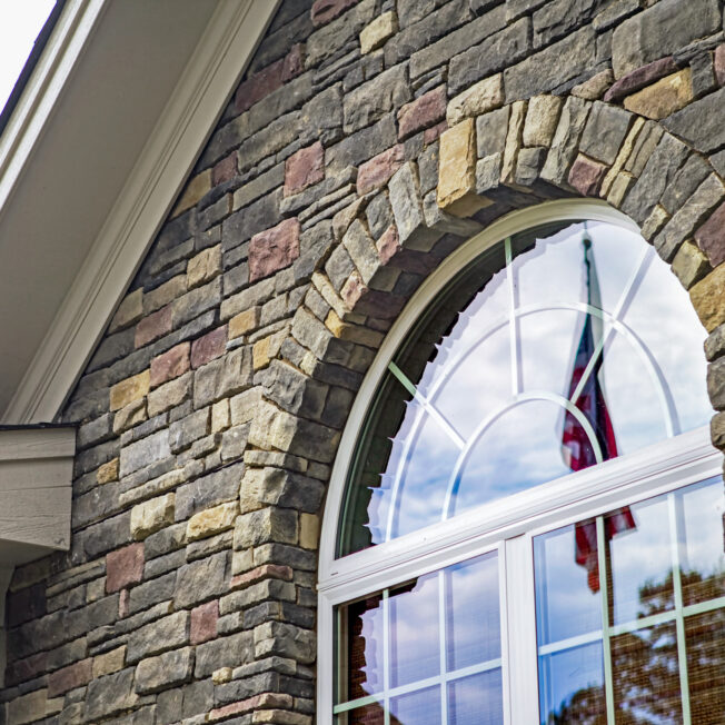 Closeup of the exterior of a home with an arch shaped window. The exterior features ProVia's Dry Stack stone veneer in the color Huron