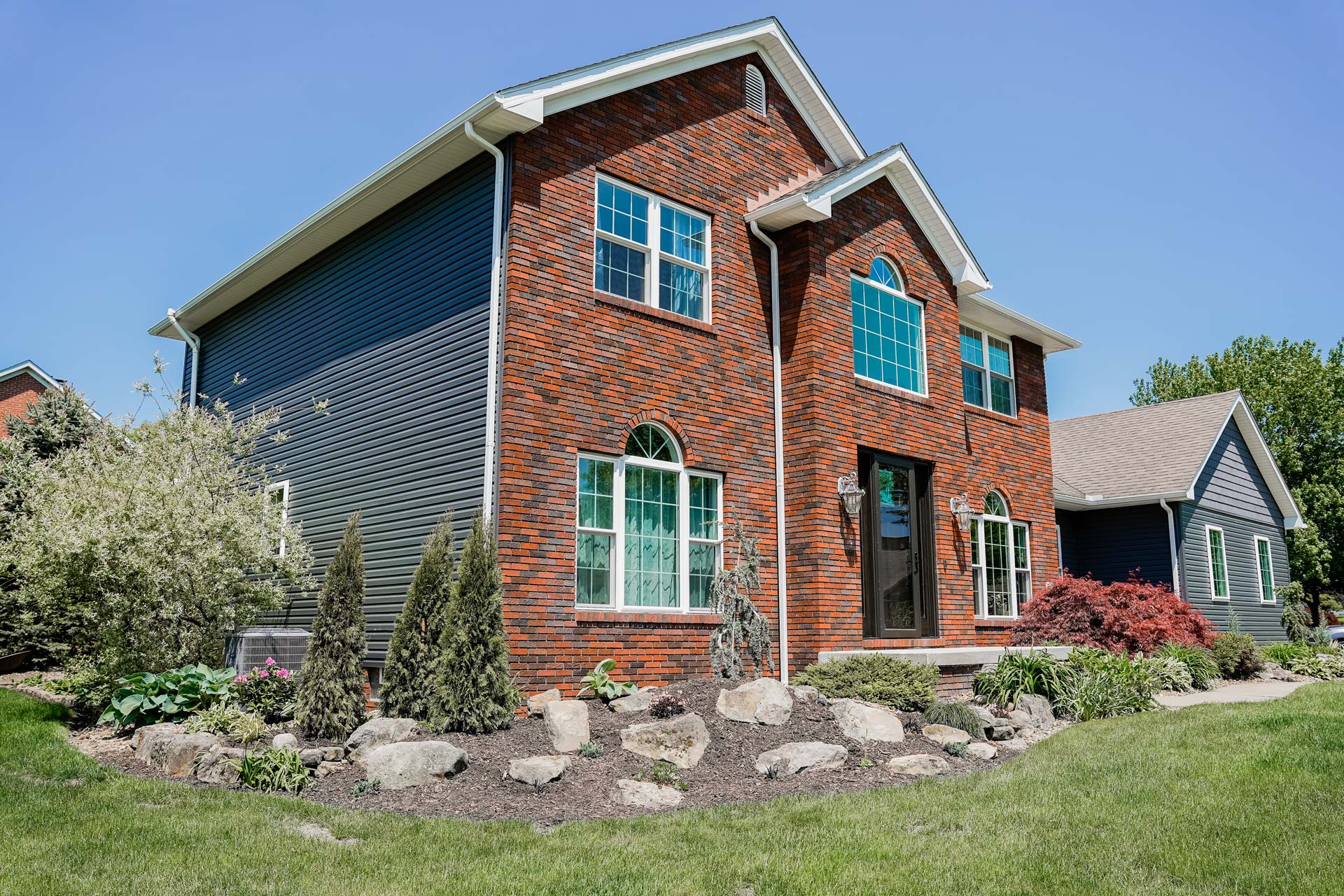 Brick two-story home with HeartTech® Vinyl Siding in Sea Slate and Endure™ Windows in White