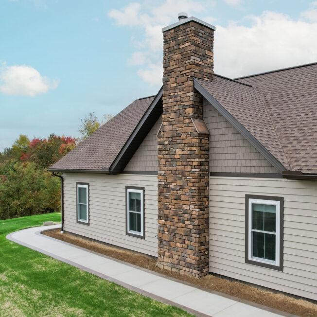 Aerial view of ProVia Harbor Mill™ Shake in Pueblo and CedarMAX® D6 Vinyl Siding in Clay on the side of a home with a chimney