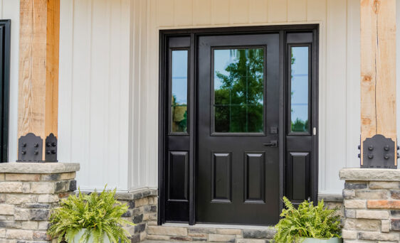 A white house with a porch with stone columns and timber and a Legacy™ Smooth 430 entry door in Coal Black with sidelites