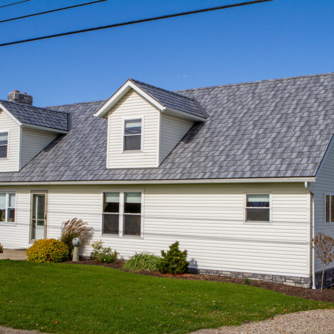Photo of a cape cod style home with gray Pepperwood Shake metal roofing—a metal shingle roof that resembles the look of shake