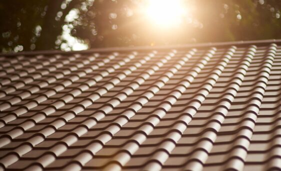 Closeup view of a home with ProVia's new metal barrel tile roof in Terracotta with the setting sun behind it, example of metal roofing that looks like clay tile