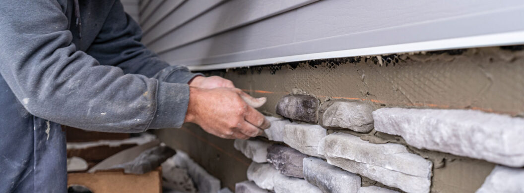 Closeup of a stone mason installing ProVia manufactured stone on a home