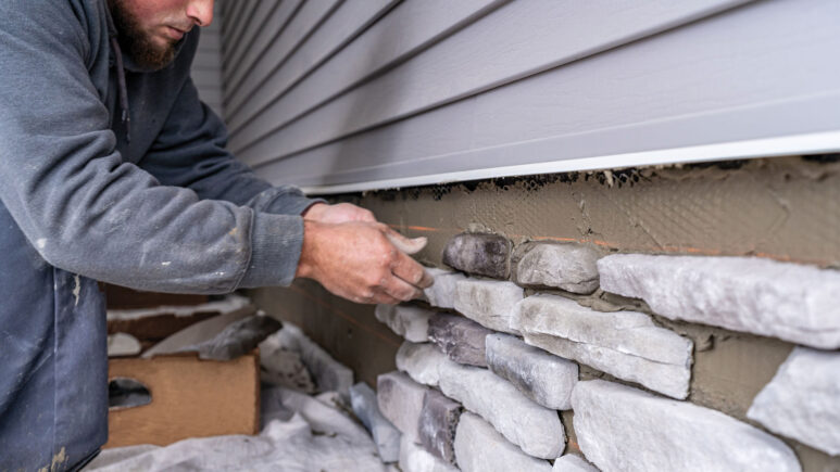 Closeup of a stone mason installing ProVia manufactured stone on a home
