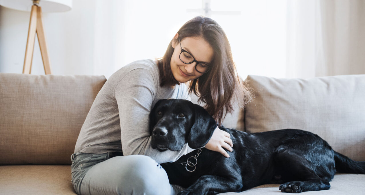 Woman cuddling black labrador dog on couch in living room on page about entry doors and storm door with built-in dog door options