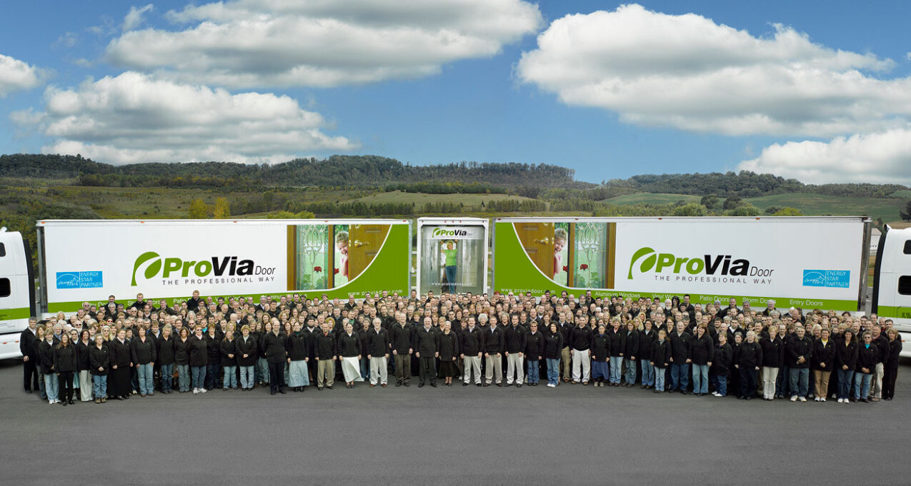 A group photo of ProVia employees in 2007 standing in front of two ProVia semi trucks