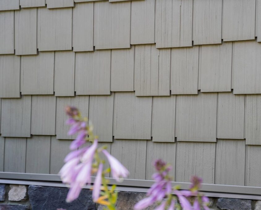 Closeup of ProVia Harbor Mill Staggered Shingle siding on a home with purple flowers in front of it