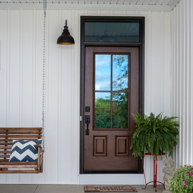 ProVia Signet® Mahogany 440-2P fiberglass farmhouse-style front door in Nutmeg with Simulated Divided Lites on a home with white board and batten, which gives the home a farmhouse exterior design look